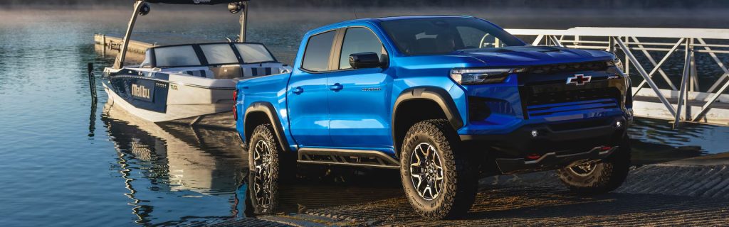 A blue Chevrolet Colorado truck parked near a boat on a dock by the water.