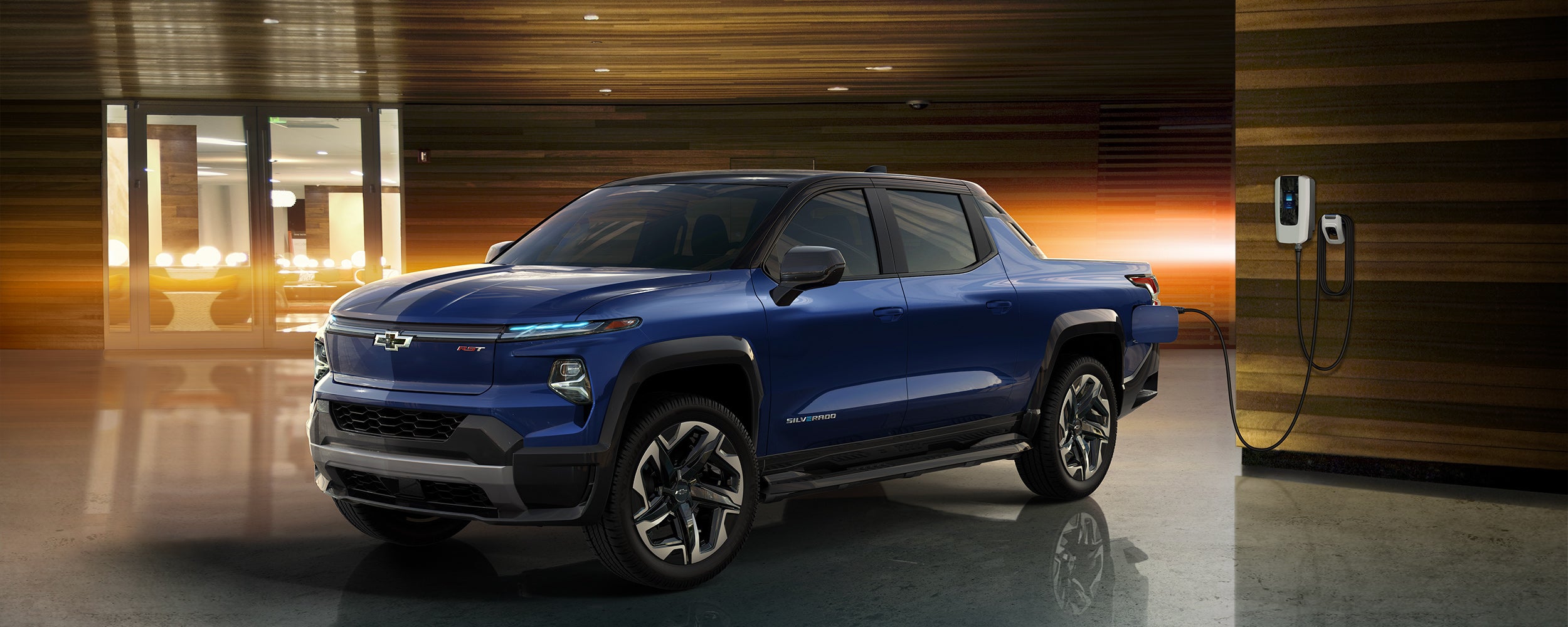 A blue Chevrolet electric pickup truck is parked in a modern setting with wood accents and ambient lighting.