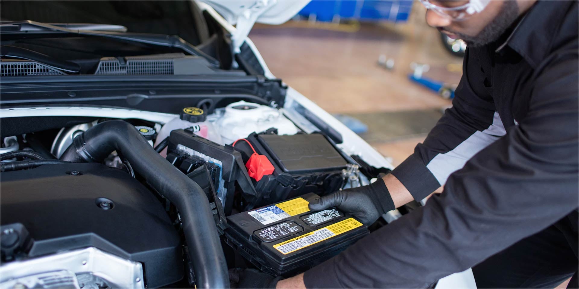 A mechanic working on a car battery under the hood of a vehicle.