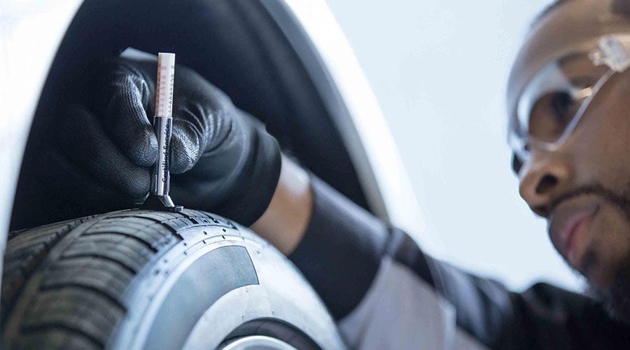 A mechanic checking the tread depth on a tire using a tread depth gauge.