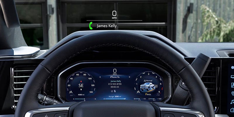 Close-up of a car dashboard display showing an incoming call from James Kelly, speedometer at 0 MPH, and vehicle information.