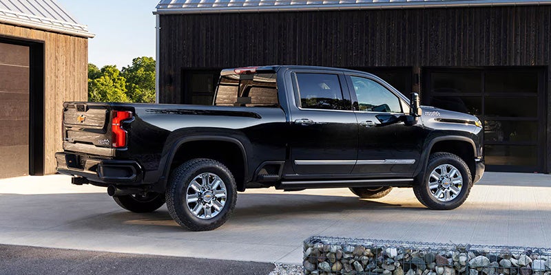 A black Silverado pickup truck parked on a driveway next to a wooden building.